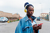 Italien, Mailand, Frau mit Kopfhörern und Smartphone in der Stadt
