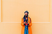 Italien, Mailand, Frau mit Gesichtsmaske, Kopfhörern und Smartphone im Freien