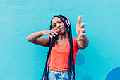 Italy, Milan, Young woman with headphones dancing in front of blue wall