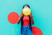 Italy, Milan, Young woman with braids blowing yellow balloon