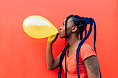 Italien, Mailand, Junge Frau mit Zöpfen bläst gelben Luftballon auf