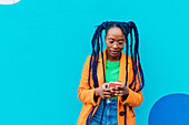 Italien, Mailand, Frau mit Zöpfen benutzt Smartphone vor blauer Wand