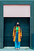 Italien, Mailand, Modische Frau mit Gesichtsmaske vor einem Gebäude
