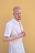 Germany, Cologne, Albino man in white shirt against yellow wall