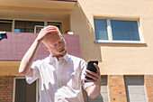 Germany, Cologne, Albino man in white shirt holding smart phone