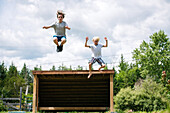 Canada, Ontario, Kingston, Boys (8-9, 14-15) jumping from wooden shelter