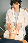 Kosmetikerin massiert das Gesicht des Patienten