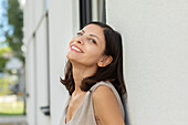 Porträt einer lächelnden Frau, die sich im Freien an eine Wand lehnt