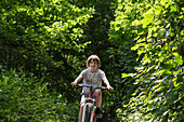 Junge fährt Fahrrad auf einem mit Bäumen gesäumten Fußweg