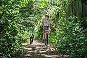 Junge fährt Fahrrad auf einem mit Bäumen gesäumten Fußweg