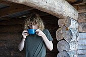 Junge (14-15) trinkt Tee in einer Blockhütte