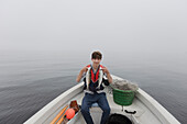 Junge (15-16) sitzt im Boot und hält einen Fisch