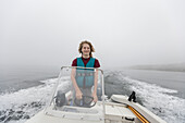 Junge (14-15) steuert Motorboot auf einem nebligen See