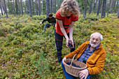 Man and two boys (14-15, 16-17) picking berries in forest