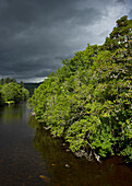 UK, Schottland, Gewitterwolken über Bäumen und Fluss