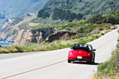 Ein rotes Cabrio fährt auf dem Highway am Meer entlang; Kalifornien, Vereinigte Staaten von Amerika