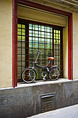 Ein Fahrrad, das vor einem Fenster mit roter Umrandung geparkt ist; Barcelona, Spanien
