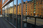 Ein braunes Backsteingebäude und eine Straße, die sich in den Fenstern eines Gebäudes spiegelt; Hamburg, Deutschland.