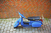 Ein motorisierter Roller, der neben einer Backsteinmauer geparkt ist; Hamburg, Deutschland