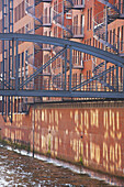 Eine metallene Fußgängerbrücke, die von einem Backsteingebäude über einen Kanal führt, mit Wendeltreppe an der Außenwand; Hamburg, Deutschland