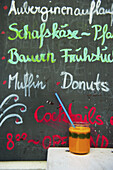 A Chalkboard Sign Advertising Food At A Restaurant And A Beverage Sitting On A Table; Hamburg, Germany