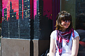 Eine junge Frau sitzt auf einer Bank neben einem bunten Wandgemälde an der Außenwand eines Gebäudes; Hamburg, Deutschland