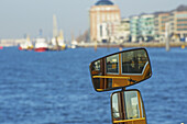 Reflexion im Spiegel der Seite eines Bootes im Wasser und Blick auf den Hafen und Gebäude am Ufer; Hamburg, Deutschland.