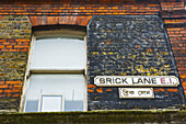 Ein Schild für die Brick Lane auf einem Backsteingebäude; London, England.