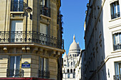 Wohngebäude mit dem Kuppeldach der Herz-Jesu-Basilika von Paris, zwischen den Gebäuden betrachtet; Paris, Frankreich.