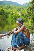 A Young Man Crouched At The Water's Edge Covered In Soap Suds; Ulpotha, Embogama, Sri Lanka