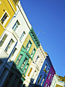 Bunte Wohnhäuser in einer Reihe entlang der Lancaster Road mit strahlend blauem Himmel; London, England