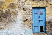 Eine alte, zerbrochene blaue Tür entlang einer rissigen Wand; Hampi, Karnataka, Indien