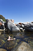 A Young Woman Swims Alone Among The Large Rocks Off Bay Of Fires Beach; Tasmania, Australia