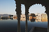 Ansicht von Gebäuden entlang der Uferlinie eines Flusses, eingerahmt von einem Torbogen; Udaipur, Indien