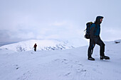 Frau und Mann wandern bei verschneitem, winterlichem Wetter den Beinn Dorain hinauf, nahe Bridge Of Orchy; Argyll und Bute, Schottland.