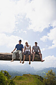 Drei Touristen sitzen auf einem Aussichtspunkt, der eine großartige Aussicht über das Tal in Laos bietet; Laos