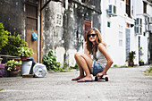 Junge Touristin mit einem Skateboard auf einer Straße in der Innenstadt; Penang, Malaysia