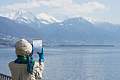 Tourist Takes A Photograph Of The Swiss Alps And Lake Maggiore On Her Tablet; Brissago, Ticino, Switzerland