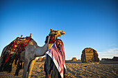 Kamel und Reiter mit Madain Saleh im Hintergrund; Madain Saleh, Saudi-Arabien