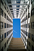 An Airplane Flying In A Blue Sky And Seen From The Ground Up The Walls Of A Residential Building; Denver, Colorado, United States Of America