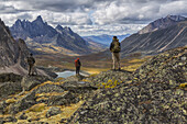 Wanderer auf Felsen mit Blick auf die farbenfrohen Täler im Tombstone Territorial Park im Herbst; Yukon, Kanada