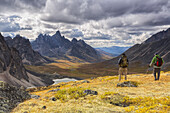 Hikers On An Overlook Viewing The Beautiful Autumn Colours In Tombstone Territorial Park, With Tombstone Mountain In The Distance; Yukon, Canada