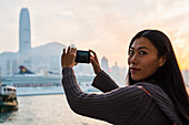 A Young Woman Photographs Buildings Across The Water, Kowloon; Hong Kong, China