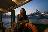 A Young Woman At The Waterfront At Sunset With A Cruise Ship In The Background, Kowloon; Hong Kong, China