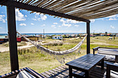 Eine überdachte Veranda mit Möbeln und einer Hängematte, und zahlreiche Gebäude entlang der Küste; Cabo Polonio, Uruguay