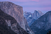 Rosa- und Lavendeltöne spiegeln sich auf El Capitan, Half Dome und Winterwolken in der Abenddämmerung im Yosemite-Nationalpark, vom Turtleback Dome aus gesehen; Kalifornien, Vereinigte Staaten von Amerika.