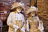 Ein Mann und eine Frau in goldenen und weißen Kostümen und Masken; Venedig, Italien.