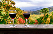 Zwei dekorative Rotweingläser stehen auf einem Holzgeländer mit Blick auf die Berge im Herbst; Fairview, North Carolina, Vereinigte Staaten von Amerika.