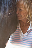 Close up of a mature woman standing next to horse head