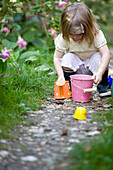 Junges Mädchen hockt in einem Garten und spielt mit Gartenspielzeug